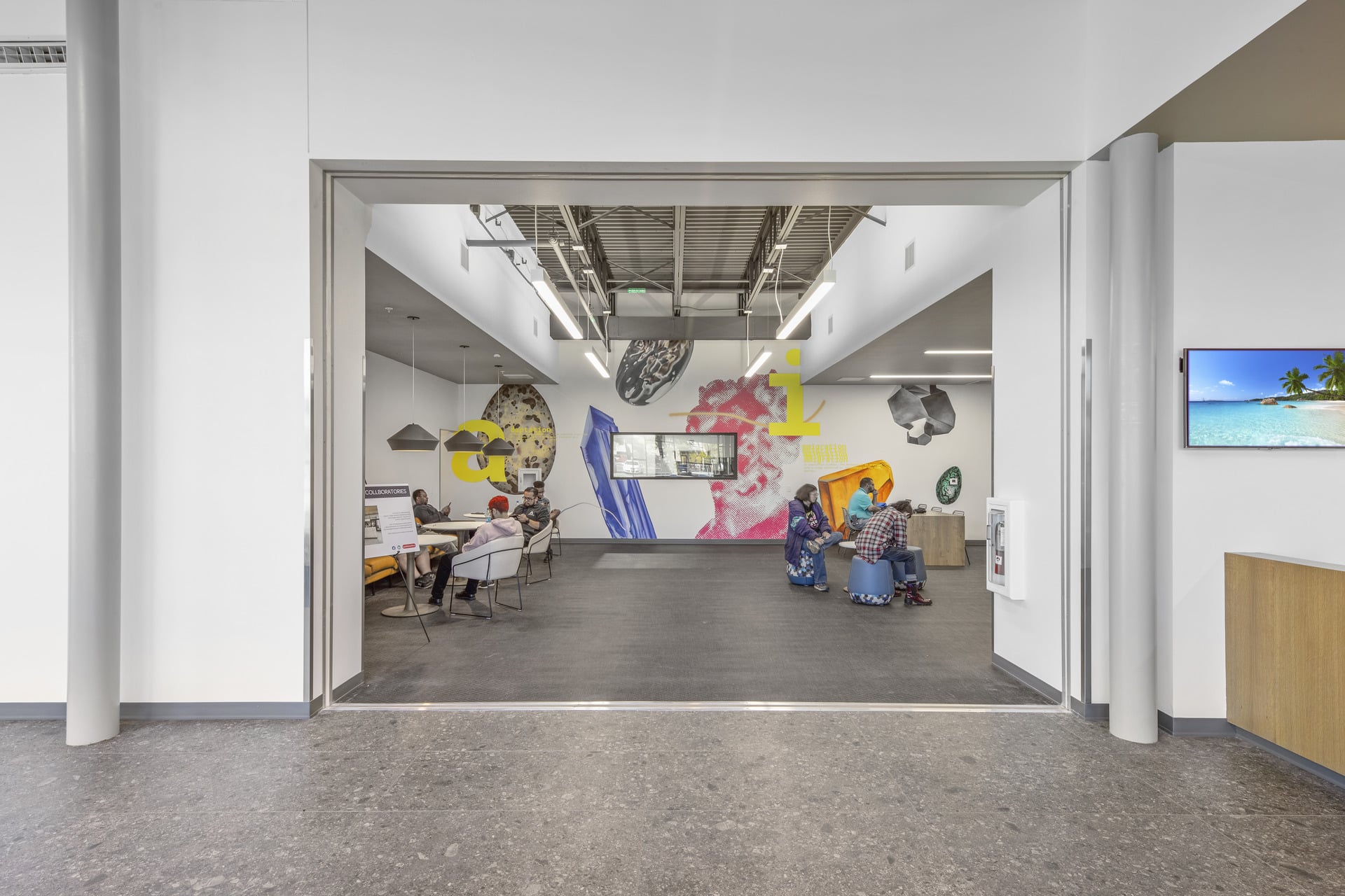 Modern interior space with people seated on stools against walls decorated with abstract art and large colorful letters.