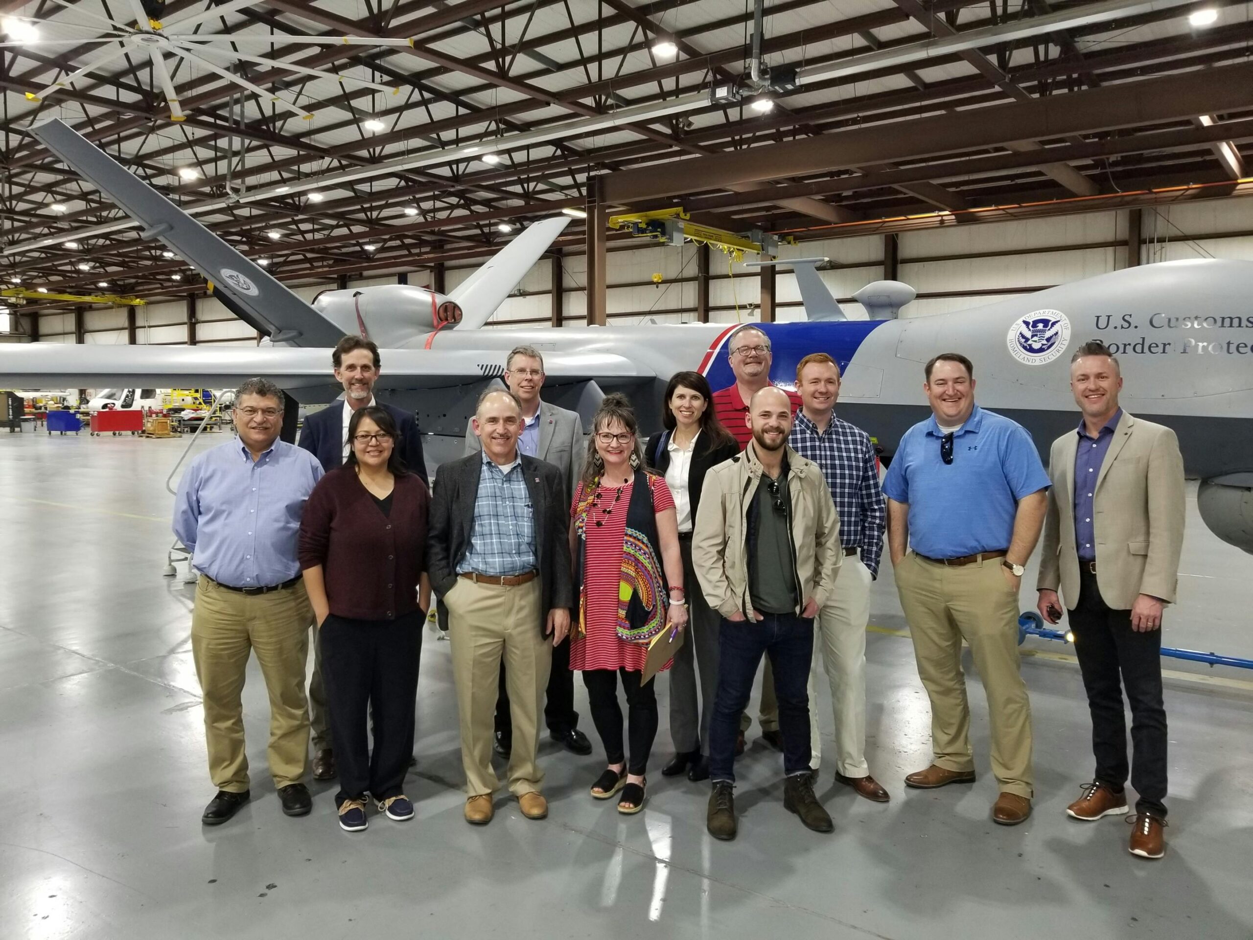 a group of coworkers in an airport hangar in front of a border patrol drone